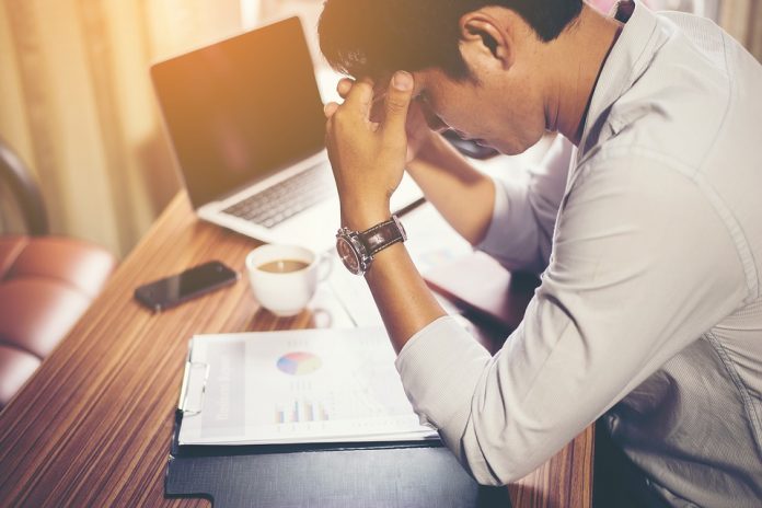 Very stressed man sitting at his desk with lots of work